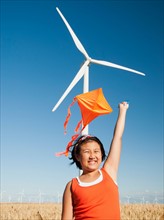 USA, Oregon, Wasco, Girls 10-11) playing with kite in wheat field, wind turbine in background.