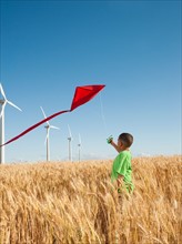 USA, Oregon, Wasco, Boy (8-9) playing with kite in wheat field, wind turbines in background.