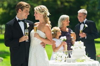 Married couple holding champagne flute, guests in background.