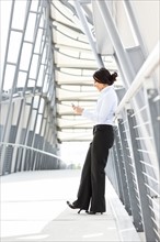 Young businesswoman on walkway, using cell phone. Photo: Take A Pix Media