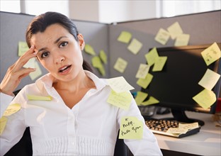 Businesswoman sitting at desk in office surrounded by adhesive notes. Photo : Jamie Grill