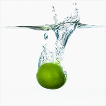 Studio shot of green apple falling into water.
