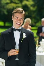 Portrait of groom holding champagne flute.
