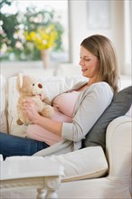 Young pregnant woman on sofa with teddy bear.