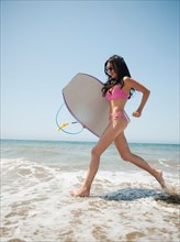 Young attractive woman running into water with swimming boards. Photo: Erik Isakson