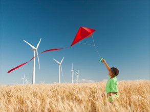 USA, Oregon, Wasco, Boy (8-9) playing with kite in wheat field, wind turbines in background.