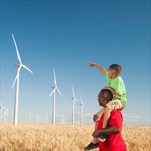 USA, Oregon, Wasco, Boy (8-9) piggy-back riding on father pointing at wind turbines. Photo: Erik