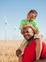 USA, Oregon, Wasco, Boy (8-9) piggy-back riding on father, wind turbines in background.