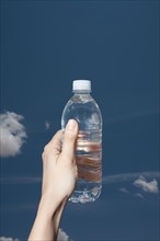 Woman's hand holding water bottle against sky. Photo : Winslow Productions
