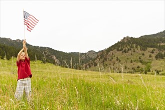 Boy (6-7) waving American flag in meadow. Photo : Shawn O'Connor