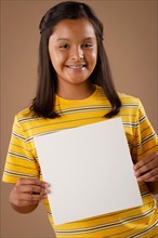 Studio portrait of girl (10-11) holding blank sheet of paper. Photo: Rob Lewine