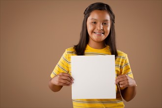 Studio portrait of girl (10-11) holding blank sheet of paper. Photo : Rob Lewine