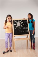 Studio portrait of two girls (8-9) standing by blackboard. Photo: Rob Lewine