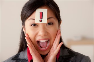 Studio portrait of businesswoman with exclamation mark sign on forehead. Photo: Rob Lewine