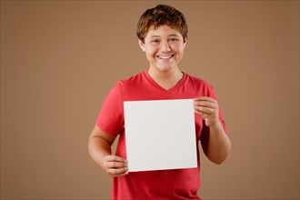 Studio portrait of boy (12-13) holding blank sheet of paper. Photo : Rob Lewine