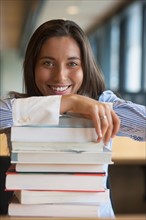 Portrait of female student leaning on stack of books. Photo : Jan Scherders