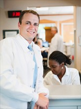 Portrait of doctor with hospital receptionist working in background.