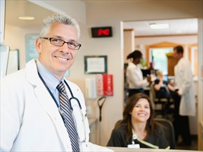 Portrait of confident doctor with female nurse in background.