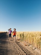 Girls (12-13, 10-11) running along dirt road.
