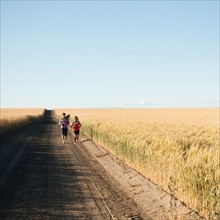 Girls (12-13, 10-11) running along dirt road.