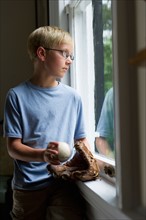 Boy holding baseball glove looking through window.