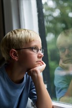 Boy (10-11) looking through window.