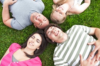 Four friends lying on grass with eyes closed. Photo : Take A Pix Media