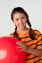 Studio portrait of girl (8-9) holding red ball. Photo: Rob Lewine