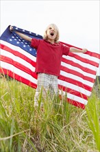Boy (6-7) waving American flag in meadow. Photo: Shawn O'Connor