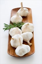 Studio shot of fresh garlic and rosemary on wooden plate.