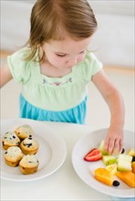 Girl (2-3) choosing between fruit salad and muffins.