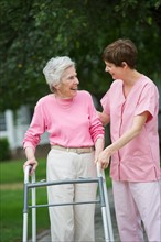 Senior woman walking with walker with help of nursing assistant.