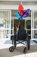 Empty wheelchair with bunch of balloons.