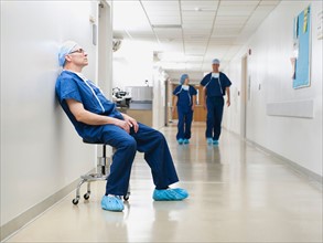 Surgeon resting in hospital corridor after operation, while two of his colleagues are walking in