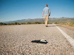 Man walking away leaving his wallet behind on empty road .