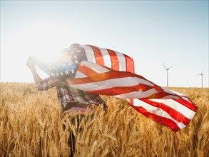 Girl (12-13) flying american flag in wheat field.