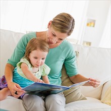 Mother with daughter (2-3) reading book on sofa.