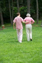 Senior woman and nursing assistant walking in back yard.