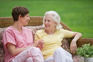 Senior woman and nursing assistant relaxing on outdoor sofa.