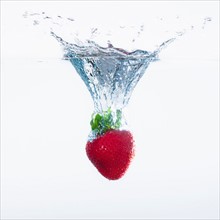 Strawberry splashing into water, studio shot. Photo : Daniel Grill