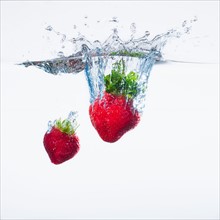 Strawberries splashing into water, studio shot. Photo : Daniel Grill