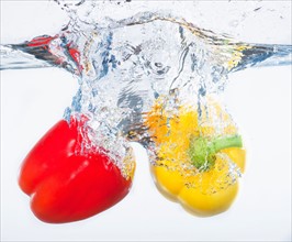 Red and yellow peppers splashing into water, studio shot. Photo : Daniel Grill
