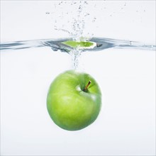 Green apple splashing into water, studio shot. Photo : Daniel Grill
