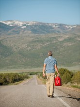 USA, Utah, Kanosh, Mid adult man carrying empty canister along empty road. Photo: Erik Isakson