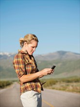 USA, Utah, Kanosh, Mid adult woman calling emergency services on empty desert road. Photo: Erik