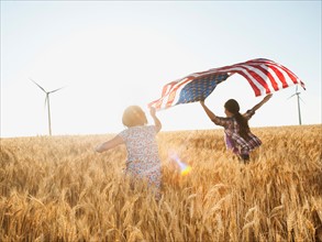 Girls (10-11, 12-13) flying american flag in wheat field.
