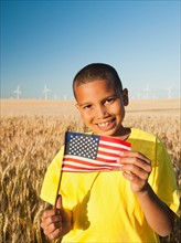 Boy (8-9) holding a small American flag in wheat field.