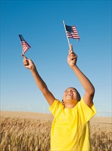 Boy (8-9) holding small american flags in wheat field. Photo: Erik Isakson