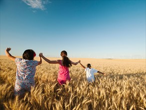 Girls (10-11, 12-13) and boy (8-9) walking though wheat field.