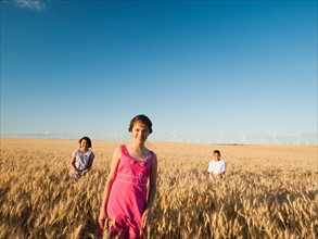 Girls (10-11, 12-13) and boy (8-9) standing in wheat field.